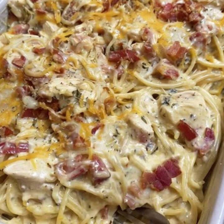 A steaming, creamy chicken spaghetti bake in a white dish with a cheese pull.