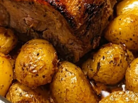 Golden garlic herb pork loin surrounded by roasted baby potatoes in a roasting pan.