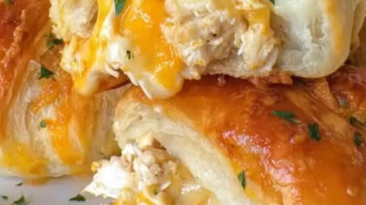 A golden-brown chicken crescent roll being lifted with a spatula, showing melted cheddar cheese.