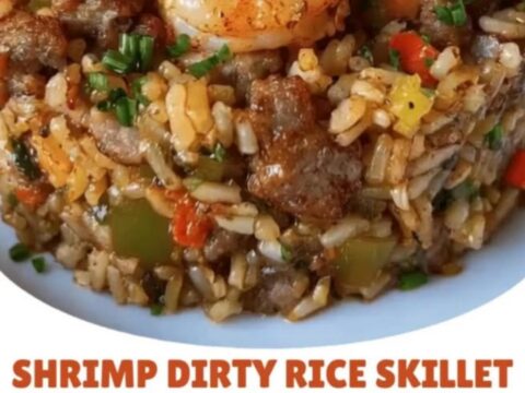 A white plate featuring cylinder-plated savory dirty rice topped with golden seared Cajun shrimp and diced chives.