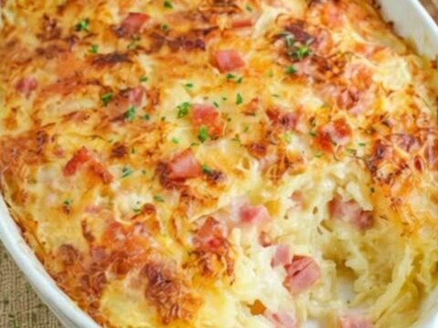 A golden, bubbly ham and hash brown casserole in a white baking dish.