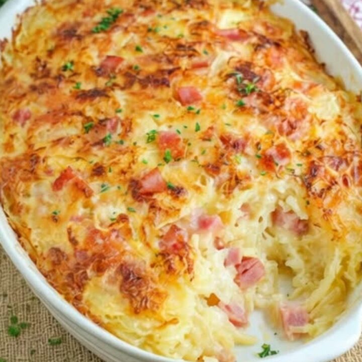 A golden, bubbly ham and hash brown casserole in a white baking dish.