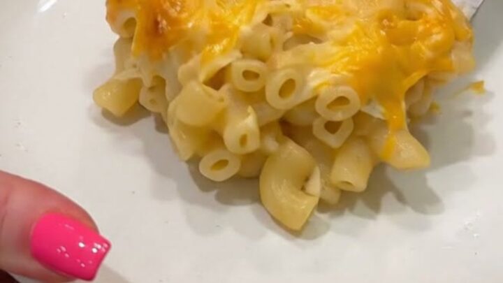 A close-up of a square of baked macaroni and cheese being lifted from a white baking dish with a metal spatula.