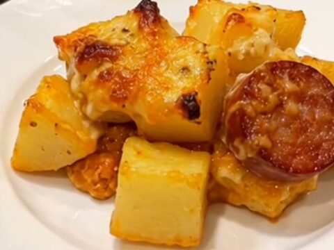 A golden, bubbly potato and sausage bake in a glass dish, fresh from the oven with melted cheese.