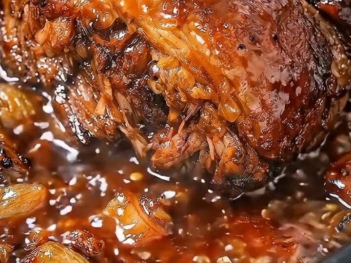 A close-up of tender, slow-cooked beef glistening in a rich garlic butter sauce inside a black slow cooker.