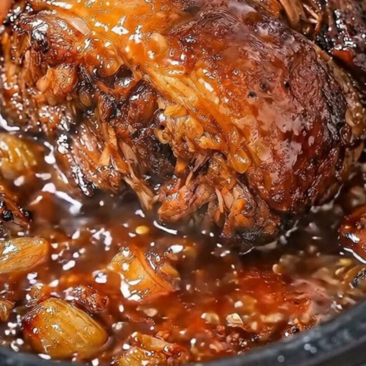 A close-up of tender, slow-cooked beef glistening in a rich garlic butter sauce inside a black slow cooker.