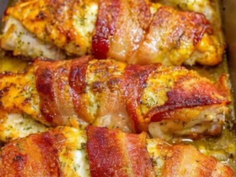 A golden, crispy bacon-wrapped chicken breast resting in a metal pan with melted parmesan cheese.