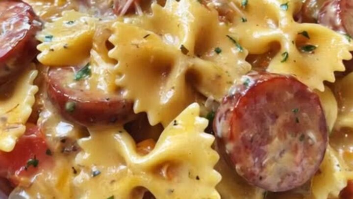 A close-up of creamy farfalle pasta with seared smoked sausage slices in a large serving bowl.