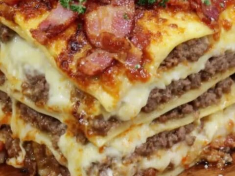 A tall slice of Parmesan Garlic Bacon Lasagna cut on a wooden board.
