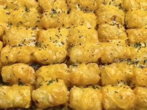 A golden, crispy tater tot casserole served in a glass baking dish with melted cheese pull.