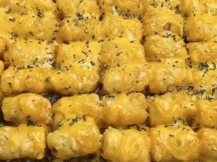A golden, crispy tater tot casserole served in a glass baking dish with melted cheese pull.