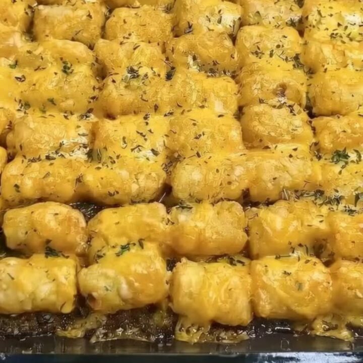 A golden, crispy tater tot casserole served in a glass baking dish with melted cheese pull.
