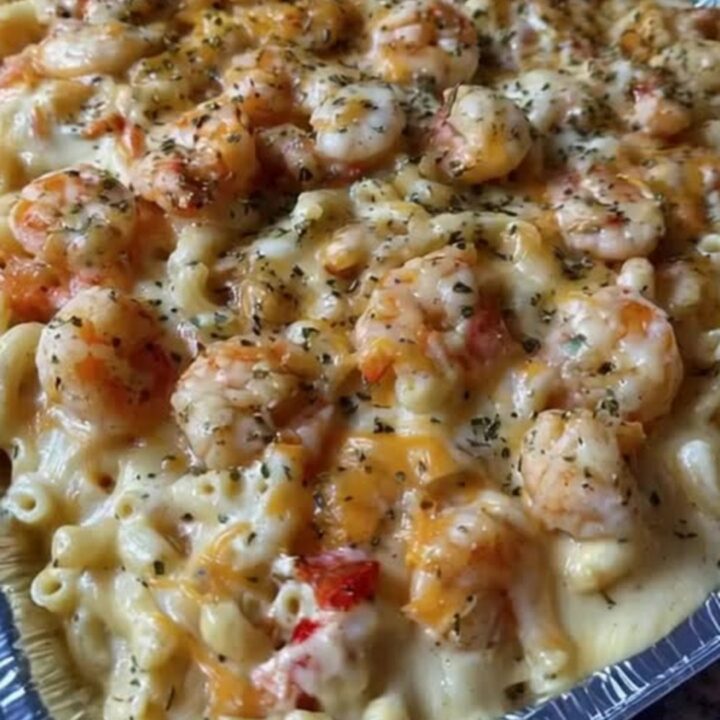 A close-up of a creamy mac and cheese bake topped with seasoned shrimp in a foil pan.