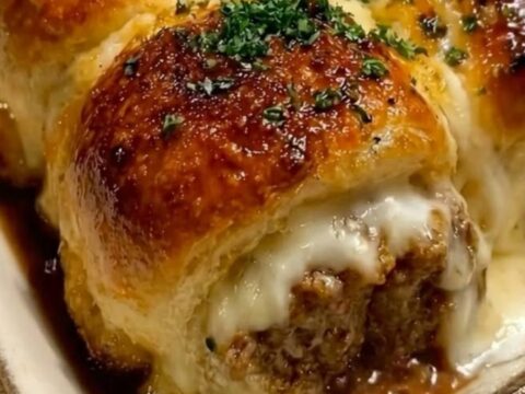 A close-up of a meatball slider being lifted from a baking dish, showing a long, gooey mozzarella cheese pull.