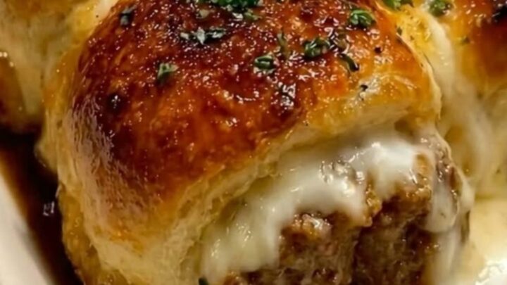A close-up of a meatball slider being lifted from a baking dish, showing a long, gooey mozzarella cheese pull.