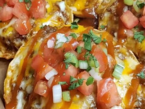 A crispy Mexican pizza with melted cheddar, seasoned beef, and fresh diced tomatoes on a white plate.