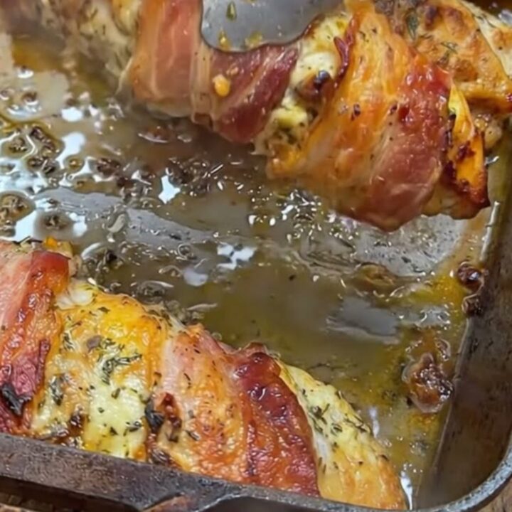 A golden, bacon-wrapped stuffed chicken breast on a plate with melted cheese visible.