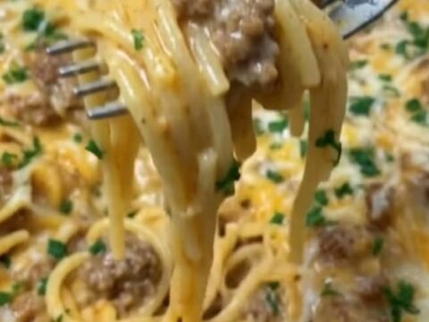 A close-up of a creamy cheddar beef spaghetti dish in a white serving bowl with fresh parsley on top.