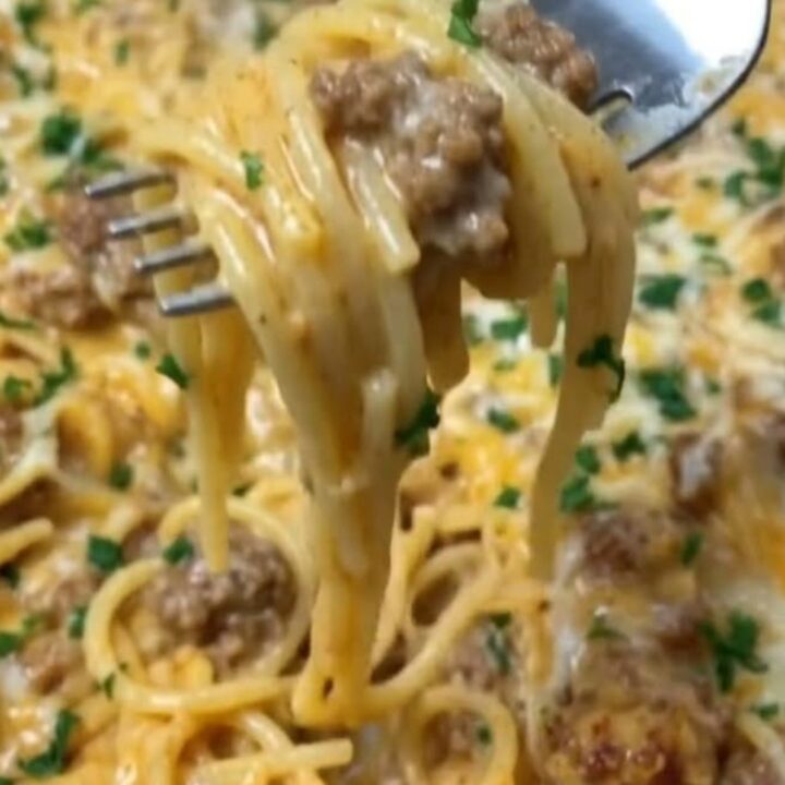 A close-up of a creamy cheddar beef spaghetti dish in a white serving bowl with fresh parsley on top.