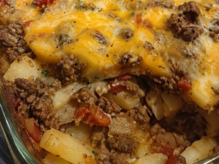 A bubbling, golden-brown cheesy hamburger potato casserole in a clear glass baking dish.