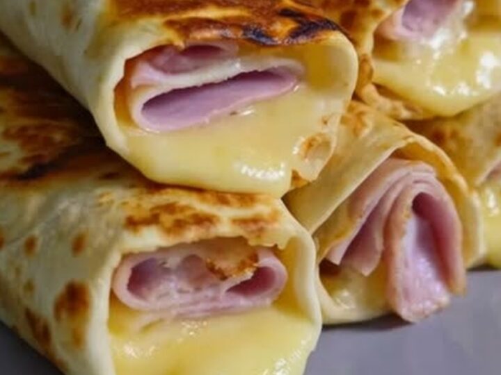 A stack of golden brown crispy ham and cheese wraps on a white plate.