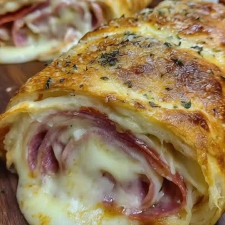 A freshly baked Italian stromboli roll sliced on a wooden board with visible melted mozzarella and layers of meat.