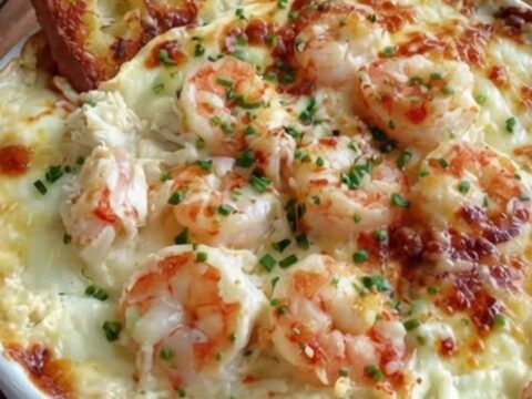 A ceramic baking dish filled with bubbly, golden-brown cheesy shrimp and crab dip.
