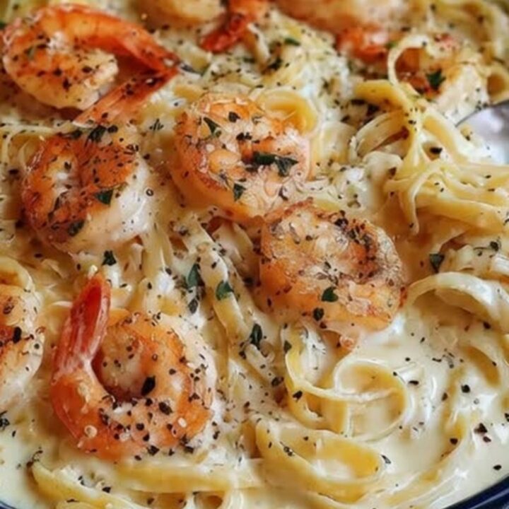 A dark bowl filled with creamy fettuccine and seared shrimp, garnished with herbs.