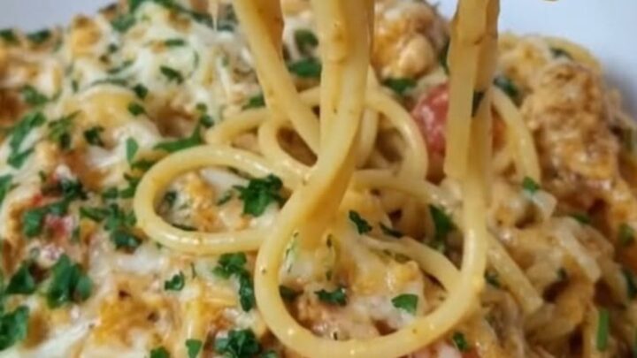 A close-up of creamy Rotel chicken spaghetti in a skillet topped with melted cheddar cheese and parsley.
