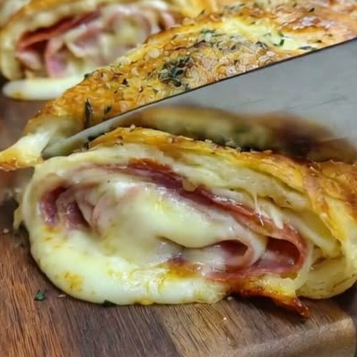 A golden-brown homemade stromboli on a wooden board, with a slice showing melted mozzarella and meat layers.