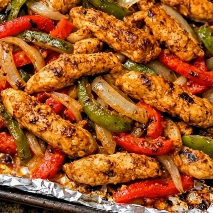 A sheet pan filled with roasted chicken strips, vibrant red and green bell peppers, and caramelized onions.