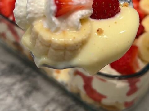 A glass dish filled with layers of creamy vanilla pudding, fresh sliced strawberries, and bananas, topped with whipped cream.