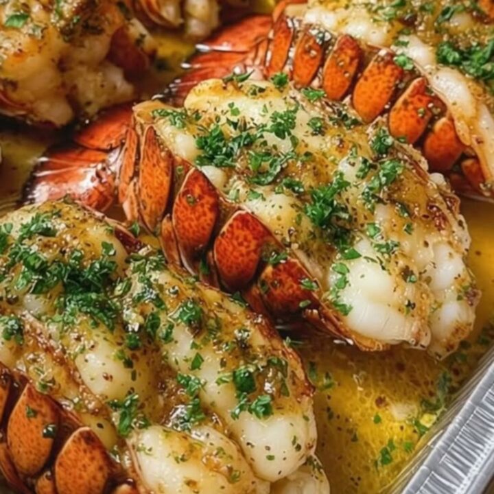 Succulent garlic butter baked lobster tails in an aluminum pan, garnished with fresh parsley.