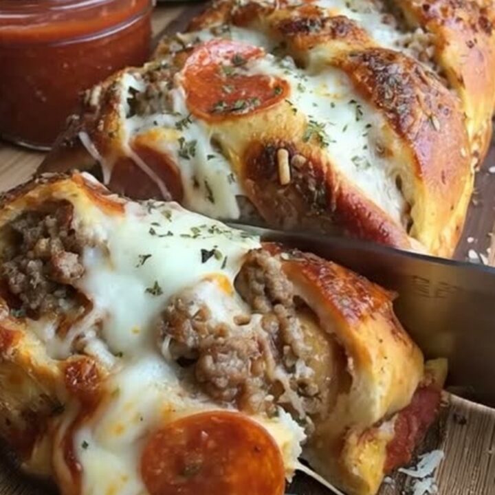 A golden-brown braided pizza bread loaf sitting on a wooden board with a side of marinara sauce.