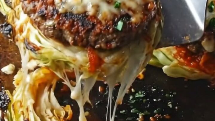 A cheesy beef-stuffed cabbage steak on a white plate with a cheese pull visible.