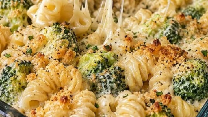 A close-up of a cheesy broccoli pasta bake in a glass dish with a long, stretchy cheese pull.