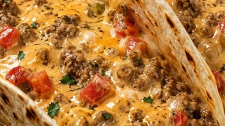A cast-iron skillet filled with a creamy, cheesy ground beef and tomato mixture with soft tortillas.