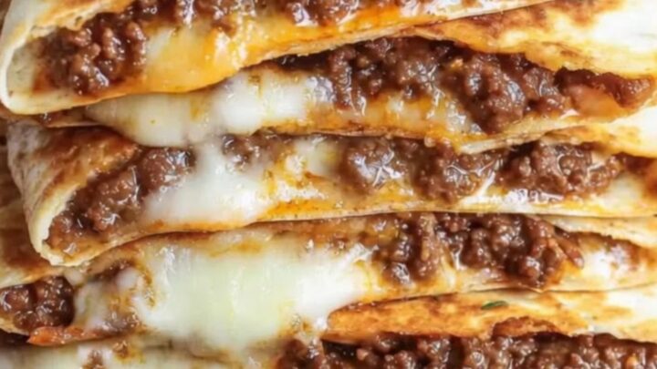 A stack of golden, crispy ground beef quesadillas on a wooden board with melted cheese stretching out.