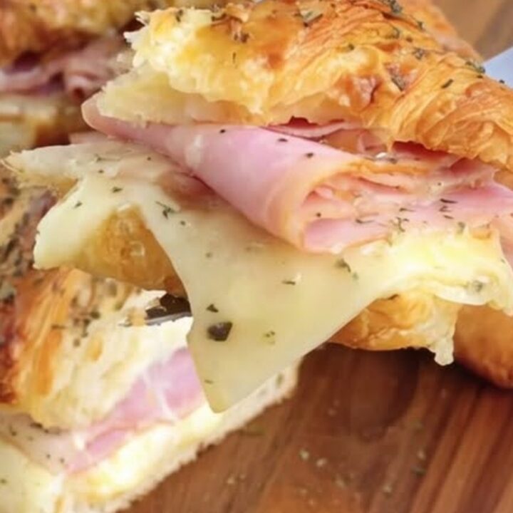 A warm, golden ham and Swiss croissant sandwich being lifted with a spatula, showing melted cheese.