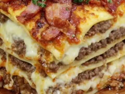 A tall, steaming slice of bacon lasagna showing layers of ground beef and melted cheese.