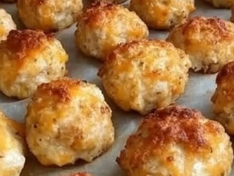 A golden-brown, crispy cheese ball being lifted from a baking sheet by metal tongs with visible steam.
