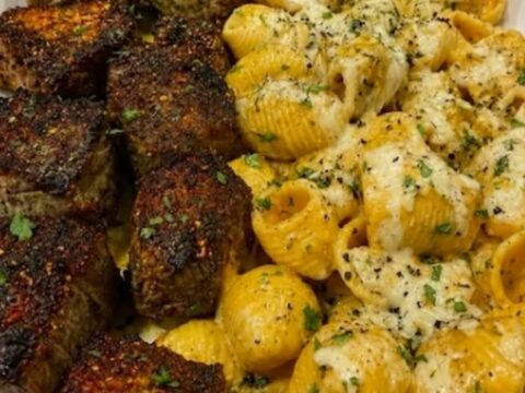 A platter filled with juicy seared steak bites and creamy shell pasta topped with melted cheese.