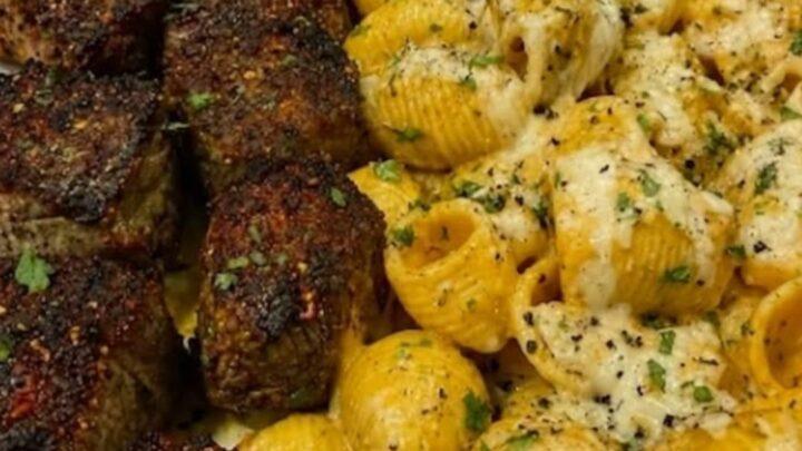 A platter filled with juicy seared steak bites and creamy shell pasta topped with melted cheese.