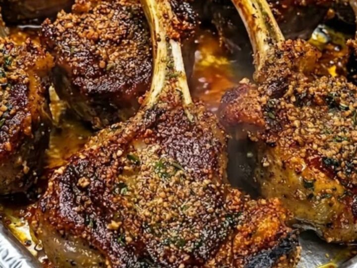 A golden herb-crusted lamb chop resting on a white plate with visible juices.