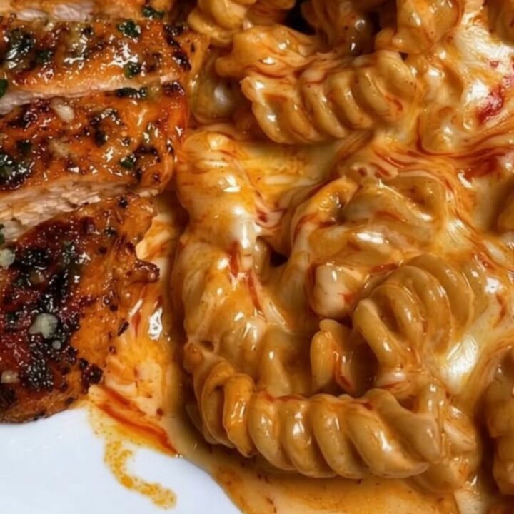 A close-up of creamy cajun rotini pasta topped with golden-brown seasoned chicken strips in a skillet.