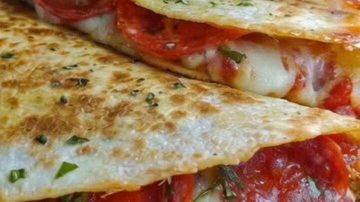A crispy pepperoni pizza quesadilla cut into wedges on a wooden board with melted cheese stretching out.