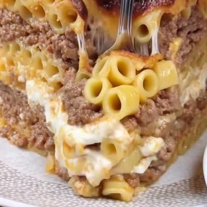 A towering slice of Greek pastitsio with clear layers of pasta, spiced beef, and a browned béchamel crust
