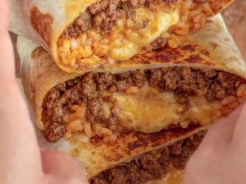A golden-toasted grilled cheese burrito resting on a wooden board with a visible crispy cheese crust.