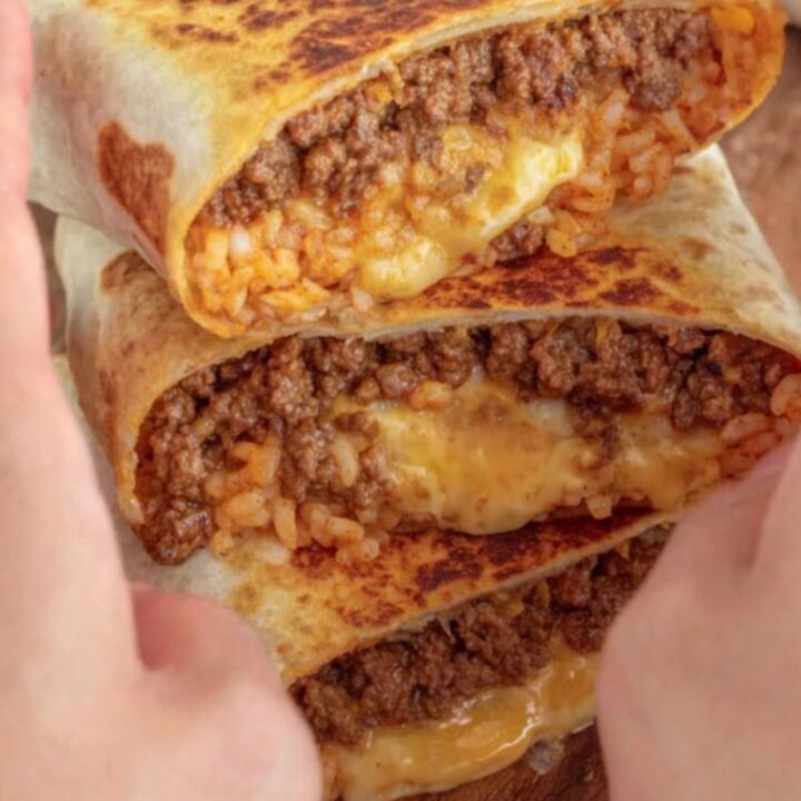 A golden-toasted grilled cheese burrito resting on a wooden board with a visible crispy cheese crust.