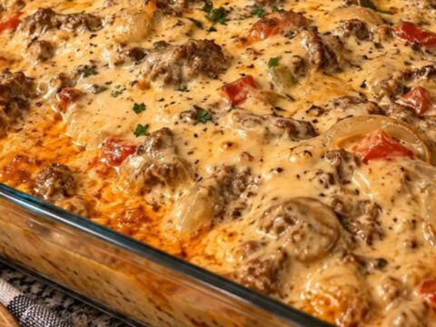 A close-up of a cheesy jerk chicken pasta bake in a glass dish with a serving spoon pulling out a portion.